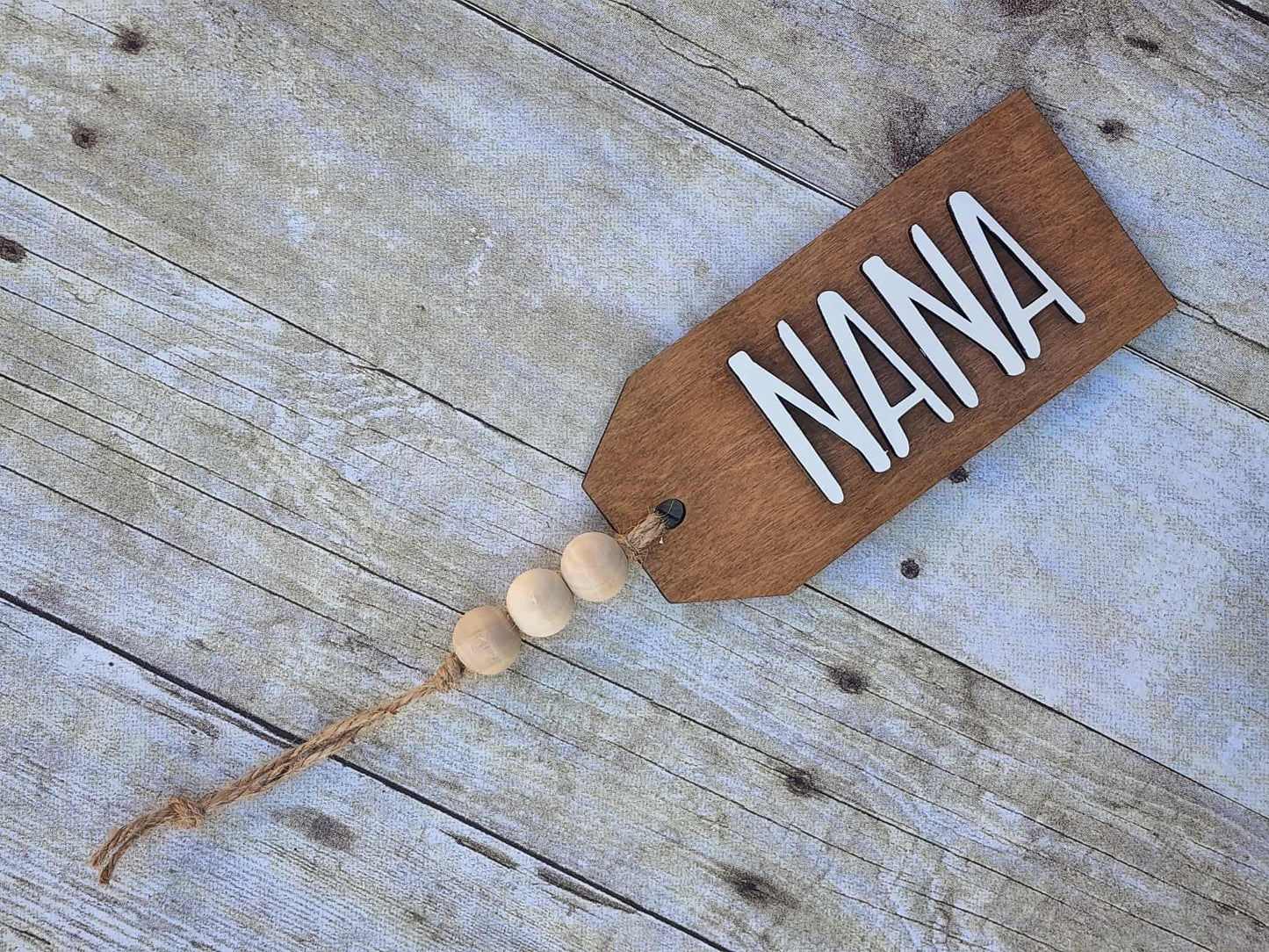 Wooden tag with 'Nana' written on it, hanging on a wooden surface.
